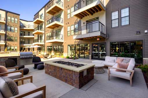 A patio area with a fire pit and seating area in front of apartment buildings. at The Cunningham Apartments, West Des Moines