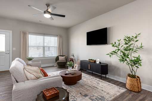 A living room with a grey couch, a brown coffee table, a TV on the wall, and a plant in a basket at Montage at Hawk Ridge Apartments, Lake St. Louis