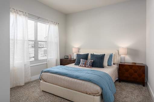 A bedroom with a bed, nightstand, and window with curtains at Hawk Ridge Apartments, Lake St. Louis, MO 