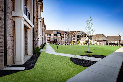 A long white walkway leads to a grassy area in front of a building.