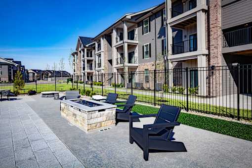 A sunny day at a modern apartment complex with a patio area featuring two lounge chairs and a fire pit.