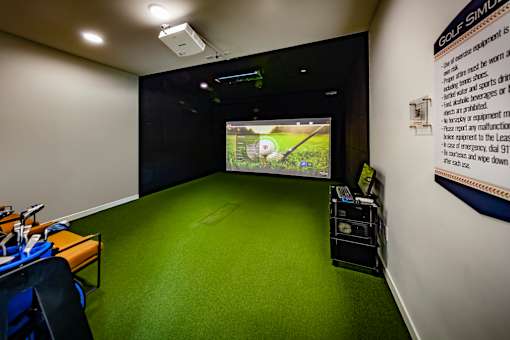 A golf simulator room with a green carpet and a screen showing a golf game.