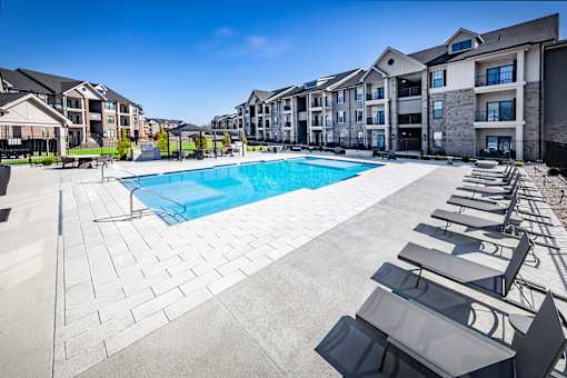 A swimming pool surrounded by sun loungers and apartment buildings.