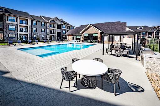 A pool area with a table and chairs in front of apartment buildings.