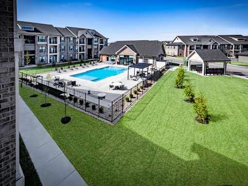 A swimming pool surrounded by a fence and a grassy area in front of apartment buildings.