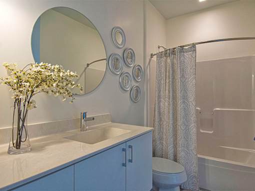 Steelcote Lofts bathroom with white cabinetry and white quartz countertops. Large circular mirror and tile at Steelcote Square, St. Louis, 63103