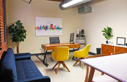 M Suites furnished office space with table, sofa and desk. Exposed brick wall and large windows