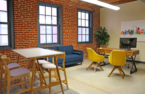 M Suites furnished office space with table, sofa and desk. Exposed brick wall and large windows