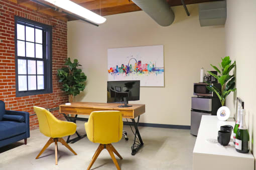 M Suites furnished office space with table, sofa and desk. Exposed brick wall and large windows