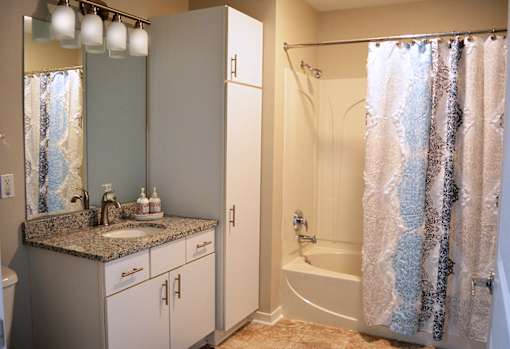 bathroom with white vanity, white cabinet and tub with shower curtain partially open at Residences at Forest Park, Missouri