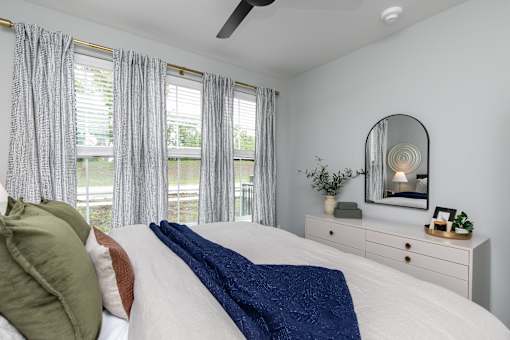 A bedroom with a bed, a dresser, and a mirror at The Cunningham Apartments, West Des Moines, IA, 50266