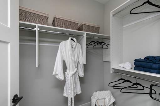 A white robe is hanging on a hanger in a closet at The Cunningham Apartments, West Des Moines