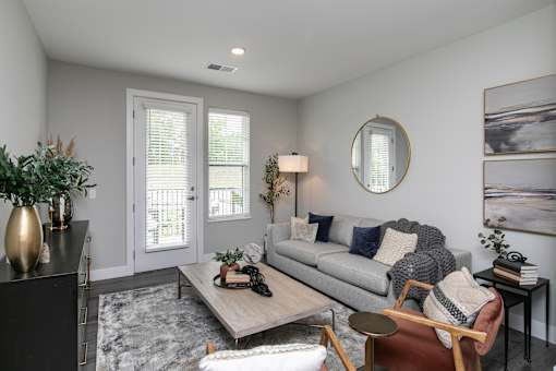 A living room with a grey couch, a coffee table, and a round mirror on the wall. at The Cunningham Apartments, Iowa