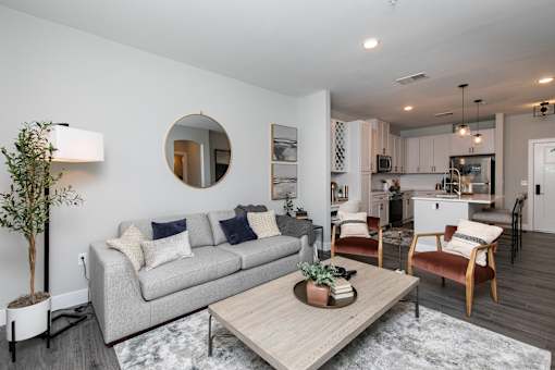 A modern living room with a grey couch, a wooden coffee table, and a round mirror on the wall. at The Cunningham Apartments, Iowa