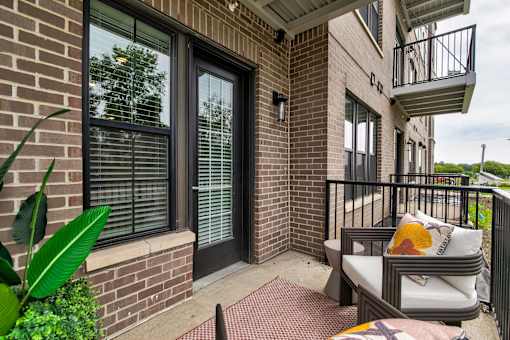 A patio with a couch and a chair is on a brick building. at The Cunningham Apartments, West Des Moines, Iowa