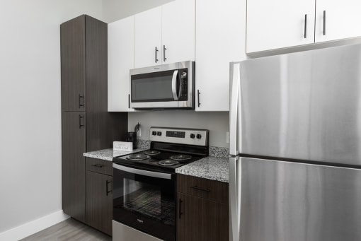 model kitchen with two- tone cabinetry, stainless steel appliances, and granite countertops  at The Residences at Delmar DivINe, St Louis