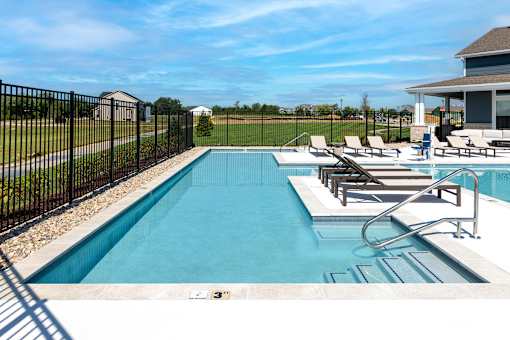 A black fence surrounds a small pool with a few chairs around it.