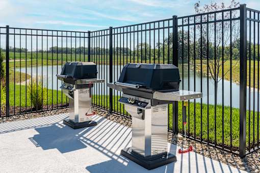 Two barbecue grills are placed on a patio with a view of a lake.