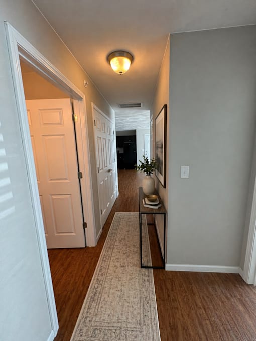 A hallway with a rug and a table with a vase on it.