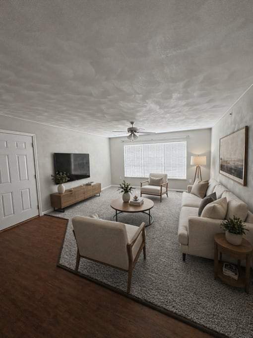 A living room with a white sofa, a wooden coffee table, and a TV on the wall.