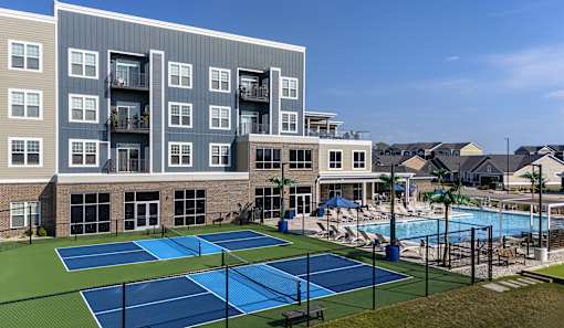 A tennis court is located in front of a large apartment building.