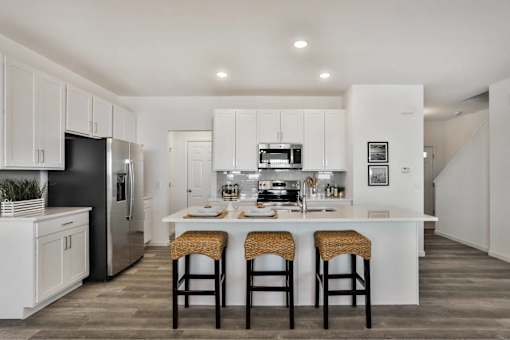 A kitchen with white cabinets and a large island with three stools.