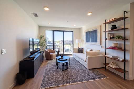 A living room with a white couch, a black coffee table, and a large window with a view of the outside.