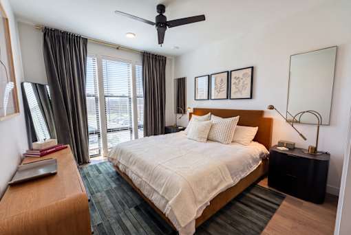 A bedroom with a large bed, a ceiling fan, and a window with curtains.