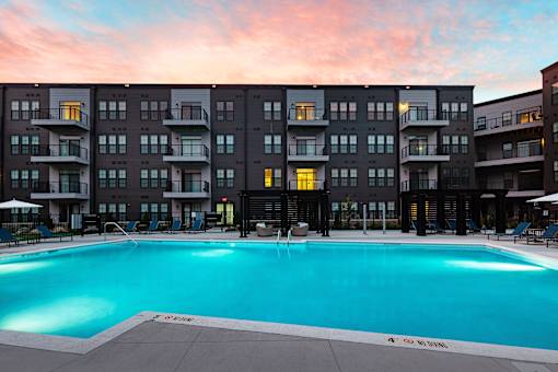 A large swimming pool in front of a building with a sunset in the background. at The Cunningham Apartments, West Des Moines, IA, 50266