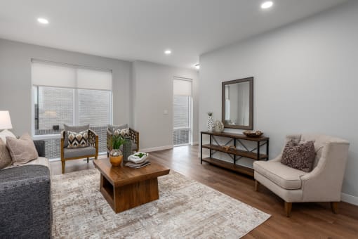living room with rich plank flooring, oversized windows with custom shades, full size sofa, two arm chairs, coffee table and end table at The Flats & Terraces at Wildhorse Village, Chesterfield, MO 63