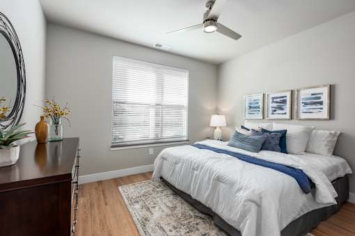 A bedroom with a bed, a dresser, a ceiling fan, and a window with blinds.