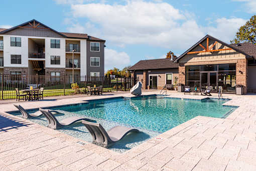 A large swimming pool with a patio and a building in the background.