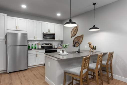 A kitchen with a refrigerator, microwave, oven, sink, and wooden chairs.