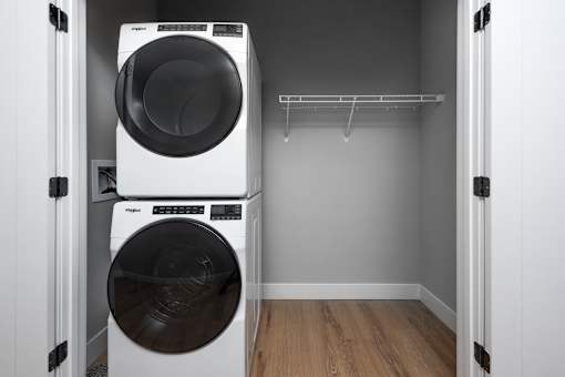 A white dryer is stacked on top of a white washer in a small laundry room.