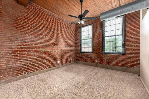 an empty room with a brick wall and a ceiling fan at Lofts at Lafayette Square Apartments, Saint Louis, Missouri