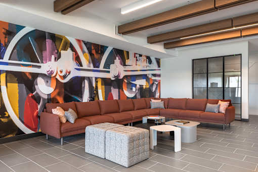 A living room with a large mural on the wall and a brown sofa.