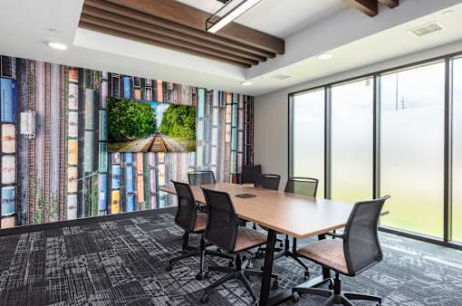 A conference room with a large table and chairs, a screen on the wall, and a window with a view of the outside.