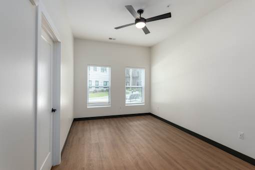 A room with a ceiling fan and two windows.