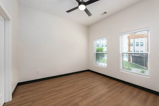 A room with a ceiling fan and two windows.