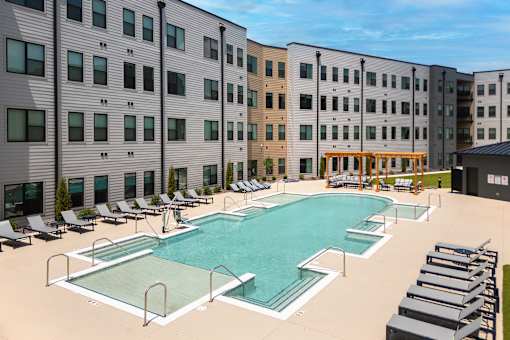 A large swimming pool surrounded by sun loungers in front of a building.