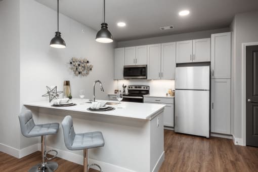 a kitchen with white cabinets and a white island with two chairs at The Station St. Peters, St. Peters, MO