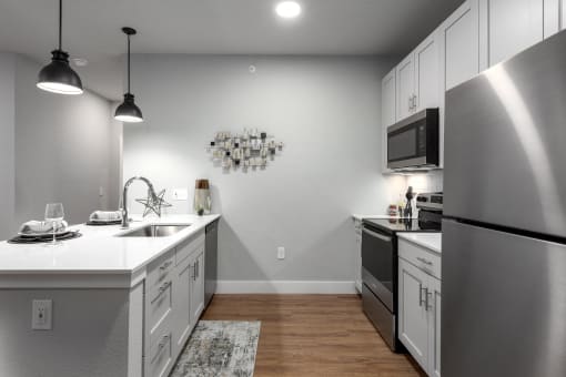 view of kitchen with stainless steel appliances and island with white counter tops and a sink at The Station St. Peters, St. Peters, MO 63376