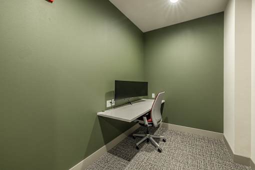 A white desk with a computer and chair in a room with green walls.