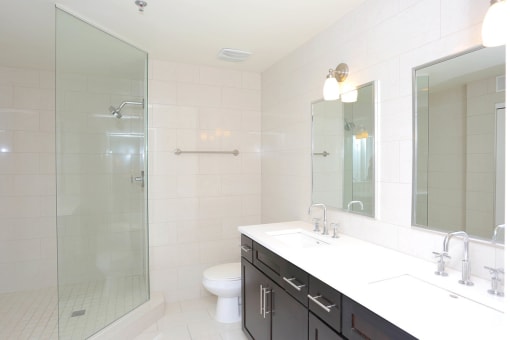 2 bedroom bathroom with dark cabinet, white vanity, mirror and stand up shower with white tile. at York House, Saint Louis, 63108