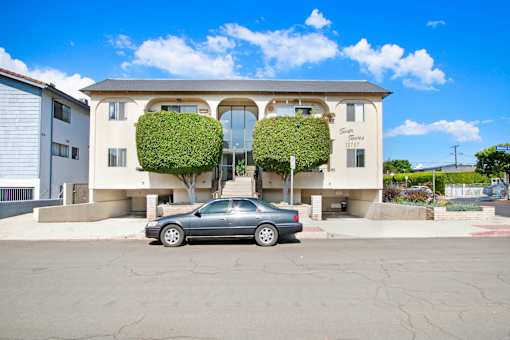 A car is parked in front of a two-story building with green plants on the front.
