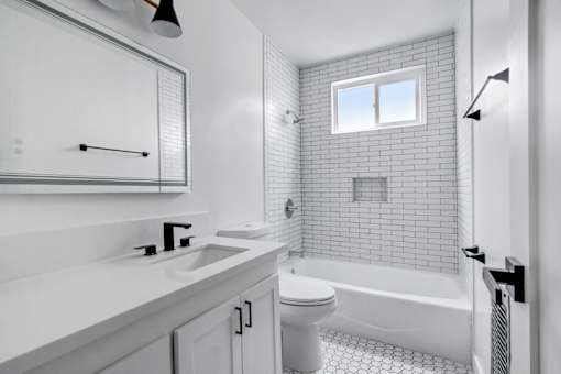 A white bathroom with a window above the bathtub.