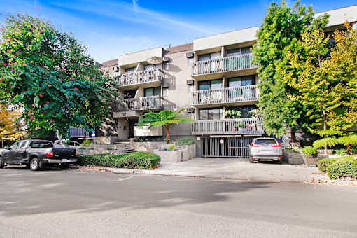 A black car is parked on the left side of a street in front of a building with balconies.