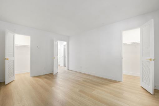 A room with white walls and wooden flooring with three open doors.