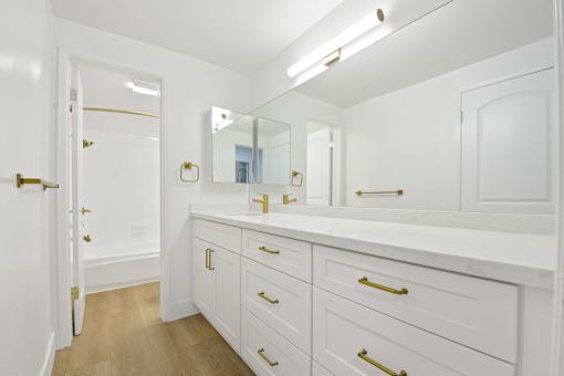 A white bathroom with a marble counter top and gold handles.