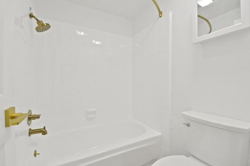 A white bathroom with a gold shower head and faucet.